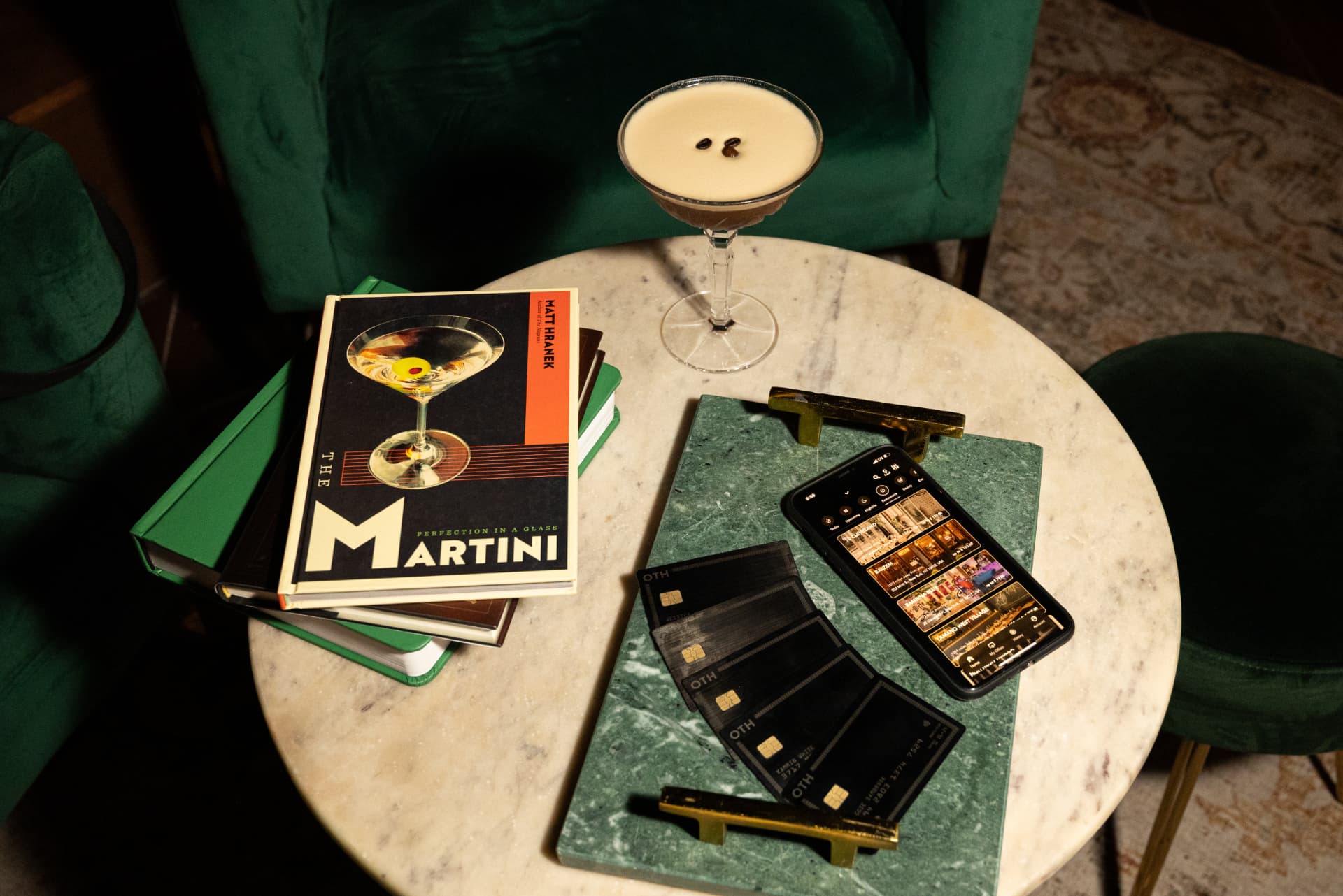An espresso martini beside a book, a phone and black member cards on a marble table